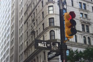 an image of a red traffic light displaying signs to wall street and broadway